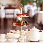 A traditional English afternoon tea, with finger sandwiches and delicate pastries displayed on a three tier stand, accompanied by a china tea service