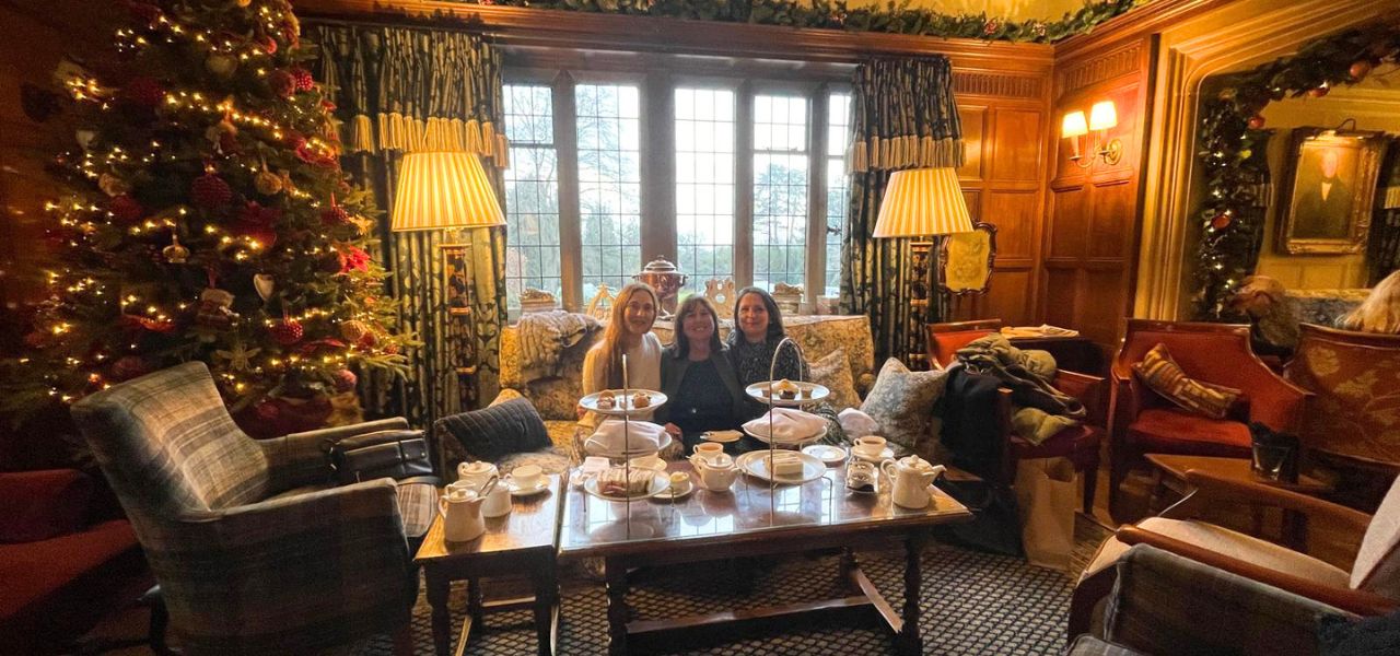 Three people sitting on a hotel lobby sofa, next to a Christmas tree. They are spending Christmas in the Cotswolds.